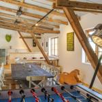 Großer Raum mit Holzdecke, Tisch, Stühle und Foosballtisch. Fenster und Lampe sichtbar.