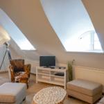 Wohnzimmer mit schrägen Dachfenstern, Sofa, Sessel und Fernseher.
