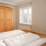 Schlafzimmer mit Holzbett, Kleiderschrank und zwei Fenstern mit Blick nach draußen.