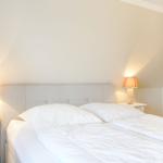 Schlafzimmer mit Bett, zwei Nachttischen und Lampen an den Seiten.