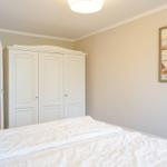 Schlafzimmer mit weißem Bett, Kleiderschrank und Leuchtturm-Bild an der Wand.