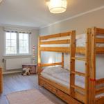 Zimmer mit Doppelstockbett und Einzelbett, Fenster, Kleiderschrank und Bodenbelag.