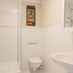 Badezimmer mit Dusche, Toilette und Waschbecken. Wandbild zeigt Leuchtturm Weserhever.