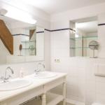 Badezimmer mit zwei Waschbecken, Spiegeln und Holzbalken an den Wänden.