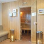 Sauna mit Holzwand, Sitzbänken und Glaswand. Nebenraum mit Sofa und Kerzen.