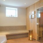 Sauna mit Holzwand und Sitzbank. Fenster, Stehlampe und Tür sichtbar.