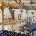 Haus mit Holzkonstruktion, Esstisch, Küchenbereich und Foosballtisch im Vordergrund.