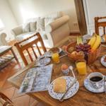 Frühstückstablett mit Obst, Brot und Getränken auf Holztisch. Im Hintergrund Sofa und Fenster.