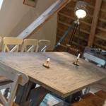 Holztisch mit Stühlen, Stehlampe und Tischkästchen in Raum mit Dachschrägen und Fachwerk.