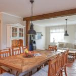 Essbereich mit Holztisch und Stühlen. Wohnbereich mit Sofa und Fenstern.