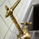 Antik-goldener Wasserhahn mit zwei Griffen über einem Küchenspülbecken.