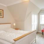 Schlafzimmer mit Doppelbett, Schrank und Sessel vor Fenster.