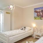 Zwei Einzelbetten mit Kuhmotiven, Wandbild und Schrank im Schlafzimmer.