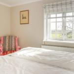 Schlafzimmer mit Bett, Fenster und Stuhl mit buntem Stoff.