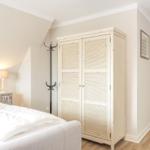 Schlafzimmer mit Bett, Kleiderschrank und Stehlampe. Durchgang zu weiteren Räumen.