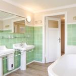 Badezimmer mit zwei Waschbecken, Badewanne und grünen Fliesen.