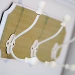 Wandhalter mit drei weißen Haken an einem grünlich-beigen Paneel.