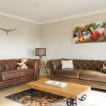 Zwei braune Ledersofas mit Kissen, Holz-Tisch und Wandbild mit Kuhmotiv.