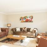Wohnzimmer mit Ledersofas, Holztisch und Wandbild mit Kuhmotiven.