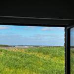 Durch das Fenster blickt man auf ein Grasfeld und einen Flughafen im Hintergrund.