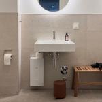 Badezimmer mit Waschbecken, Spiegel, Holzbank und Toilette.