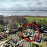 Dorfhaus mit Strohdach und Garten, Blick auf Wasser und Wiesen.