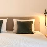 Ein Bett mit weißer Bettwäsche, grünen Kissen und einer Wandlampe.