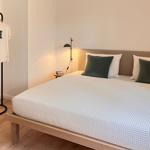 Ein Bett mit weißer Bettwäsche und grünen Kissen. Eine Lampe und ein Kleiderständer sind sichtbar.