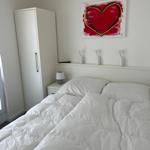 Schlafzimmer mit weißem Bett, Kleiderschrank und Wandbild mit Herz.