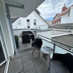 Terrasse mit Sitzgruppe, Tisch und Pflanze. Blick auf Dächer und Gebäude.