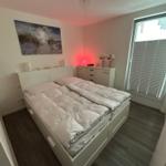 Schlafzimmer mit weißem Bett, Wandbild und Fenster mit Jalousie.