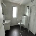 Badezimmer mit Dusche, WC und Waschbecken. Weiße Fliesen und dunkle Bodenfliesen.
