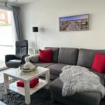Ein Wohnzimmer mit grauem Sofa, roten Kissen und einem weißen Couchtisch.