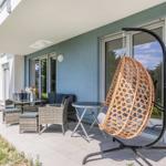 Terrasse mit Hängesessel, Sitzgruppe und Grill. Glasfront und blauer Putz sichtbar.