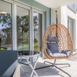 Terrasse mit Hängesessel, Tisch und Stuhl. Glasfront und Garten im Hintergrund.
