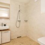 Badezimmer mit Dusche, Waschbecken und Toilette. Wand- und Bodenfliesen in hellen Tönen.