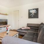Wohnzimmer mit grauem Sofa, Holztisch und Fernseher an der Wand.