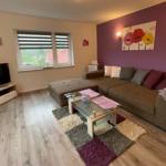 Wohnzimmer mit Sofa, Glas-Tisch und Fernseher. Wand in Lila mit Blumenbild.