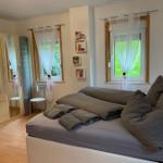 Schlafzimmer mit Doppelbett, Kleiderschrank und zwei Fenstern mit weißen Vorhängen.