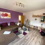 Wohnzimmer mit Sofa, Couchtisch und Wandbild an lila Wand.