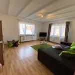 Wohnzimmer mit Sofa, Fernseher und Holzboden. Grüner Teppich und Fenster mit Vorhängen.