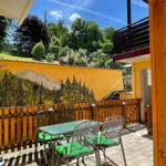 Terrasse mit Tisch, Stühlen und grünen Kissen. Hintergrund: gelbe Wand mit Waldmotiv.