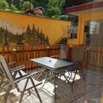 Terrasse mit Tisch und Stühlen, gelber Wand mit Waldmalerei, Holzgeländer und Hinterhof.