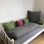 Ein Bett mit grauer Bettwäsche, grünen und rosa Kissen sowie gefalteten Handtüchern.