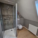 Duschbad mit Dusche, Toilette und Fenster. Holzfußboden und graue Wände.