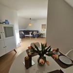 Essbereich mit Tisch und Stühlen, im Hintergrund Wohnbereich mit Sofa und Couchtisch.