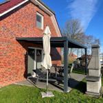 Roter Backsteinbau mit Terrasse, Sonnenschutz und Gartenmöbeln unter klarem Himmel.