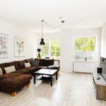 Wohnzimmer mit braunem Sofa, Holzboden und Fenstern zum Garten