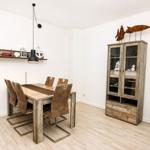 Esszimmer mit Holztisch, Stühlen und Sideboard. Wandregal und Dekoration sichtbar.