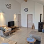 Wohnzimmer mit Sofa, Fernseher und Kaminofen. Holzmöbel und Wanduhr sichtbar.